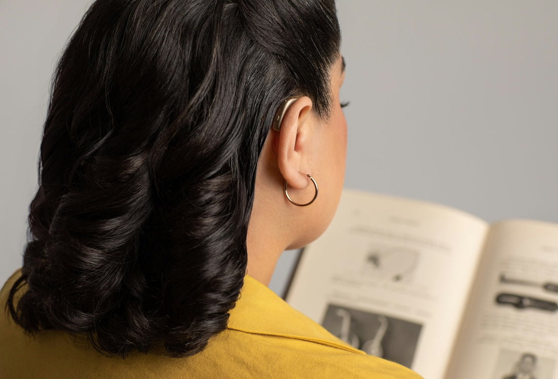 Woman wearing a hearing aid while reading a book, demonstrating the comfort and functionality of hearing aids in daily activities