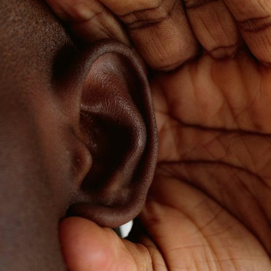 Close-up of an ear being cupped to hear better, highlighting the need for hearing aid solutions